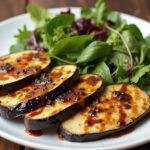 Plato de berenjena blanca asada con glaseado balsámico y ensalada fresca.