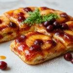Una Coca de San Juan esponjosa, decorada con frutas confitadas en colores vibrantes, espolvoreada con azúcar glass y presentada sobre un plato blanco, resaltando su textura ligera y aireada.